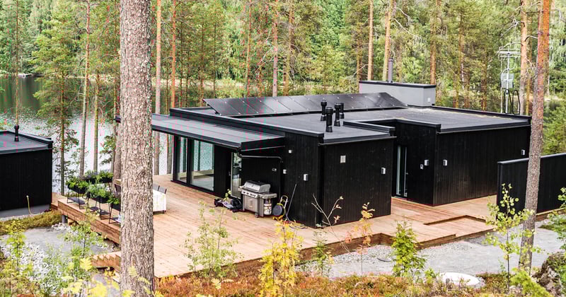 Aurinkopaneeleilla varustettu, tumma kesämökki järven rannalla.