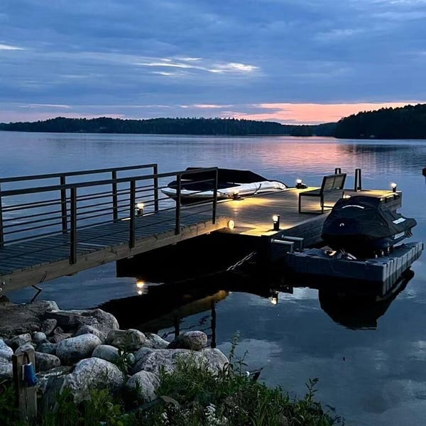 Laiturivaloilla varustettu pontonilaituri järven kannalla iltahämärän aikaan.